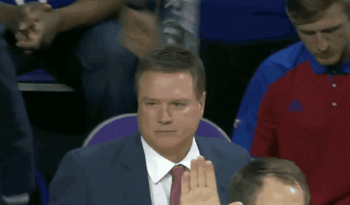 A Man In A Suit And Tie Holds Up His Hand GIF