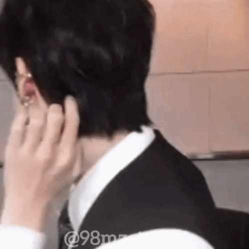 A Man In A Suit And Tie Is Adjusting His Earring While Talking On A Cell Phone . GIF