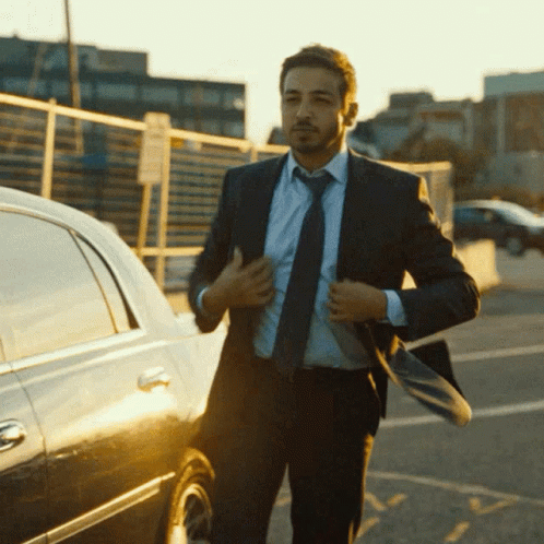 A Man In A Suit And Tie Is Adjusting His Jacket GIF