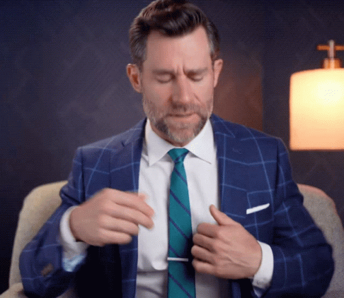 A Man In A Suit And Tie Is Adjusting His Shirt GIF
