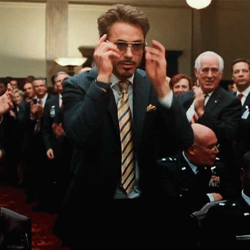A Man In A Suit And Tie Is Adjusting His Sunglasses In Front Of A Crowd GIF