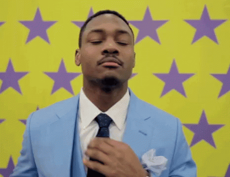 A Man In A Suit And Tie Is Adjusting His Tie In Front Of A Yellow Background With Purple Stars . GIF