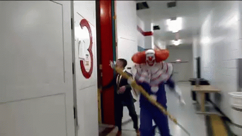 A Man In A Suit And Tie Is Being Attacked By A Clown In A Hallway . GIF
