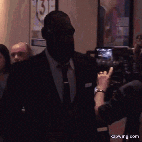 A Man In A Suit And Tie Is Being Photographed By A Woman With The Website Kapwing.com Visible GIF