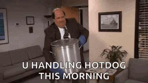 A Man In A Suit And Tie Is Carrying A Large Pot Of Hotdog In A Living Room . GIF