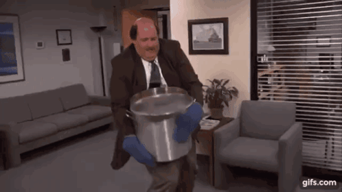 A Man In A Suit And Tie Is Carrying A Large Pot Of Water . GIF