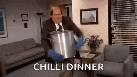 A Man In A Suit And Tie Is Carrying A Pot Of Chili Dinner In A Living Room . GIF