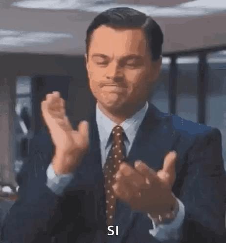 A Man In A Suit And Tie Is Clapping His Hands And Saying `` Si '' . GIF