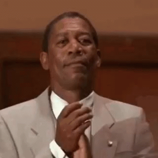 A Man In A Suit And Tie Is Clapping His Hands In A Courtroom . GIF