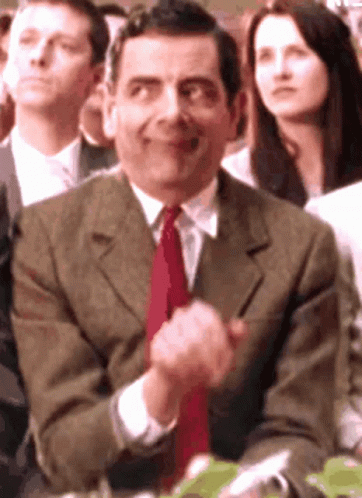 A Man In A Suit And Tie Is Clapping His Hands In A Crowd GIF
