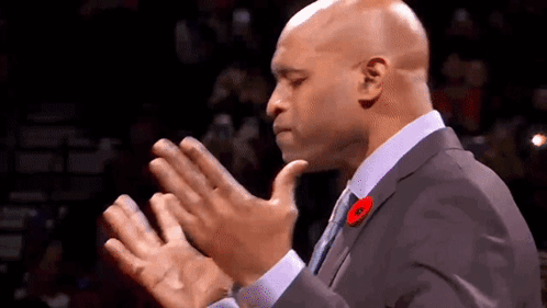 A Man In A Suit And Tie Is Clapping His Hands In A Crowd . GIF