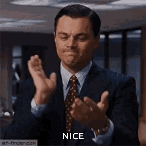 A Man In A Suit And Tie Is Clapping His Hands In A Room . GIF