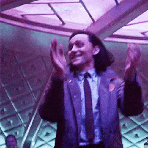 A Man In A Suit And Tie Is Clapping His Hands In A Room With Purple Lights . GIF