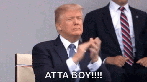 A Man In A Suit And Tie Is Clapping His Hands While Sitting In Front Of Another Man . GIF