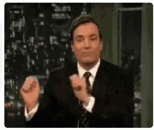 A Man In A Suit And Tie Is Clapping His Hands While Standing On A Stage . GIF