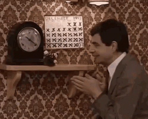 A Man In A Suit And Tie Is Clapping In Front Of A Clock And A Calendar On A Shelf . GIF