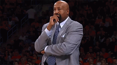 A Man In A Suit And Tie Is Covering His Mouth With His Hand While Standing On A Basketball Court . GIF
