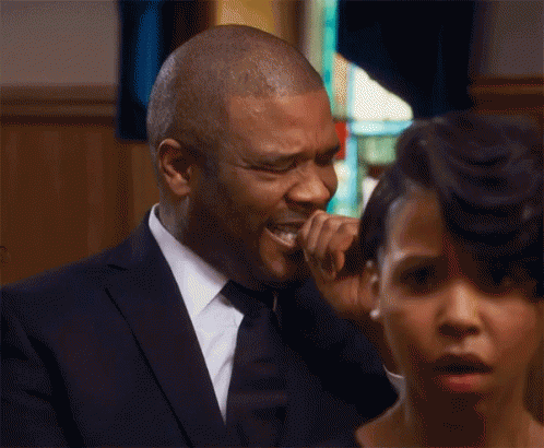 a man in a suit and tie is crying at a funeral while a woman looks on .