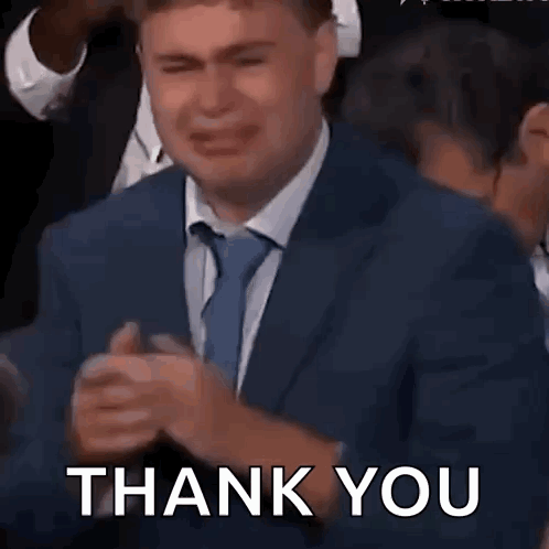 A Man In A Suit And Tie Is Crying In A Crowd And Saying Thank You . GIF