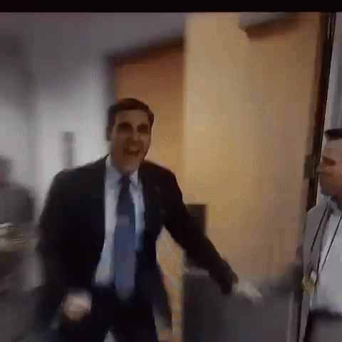 A Man In A Suit And Tie Is Dancing In A Room While Another Man Watches . GIF