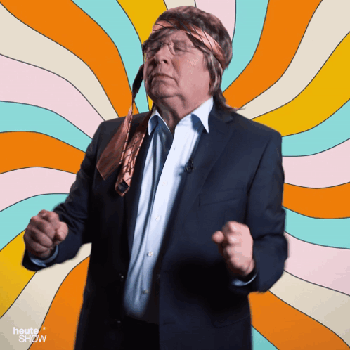 A Man In A Suit And Tie Is Dancing In Front Of A Colorful Background With The Words Heute Show On It GIF