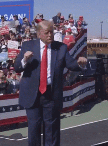 A Man In A Suit And Tie Is Dancing In Front Of A Crowd With A Sign That Says Again GIF