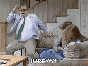 A Man In A Suit And Tie Is Dancing In Front Of A Group Of People On A Couch . GIF