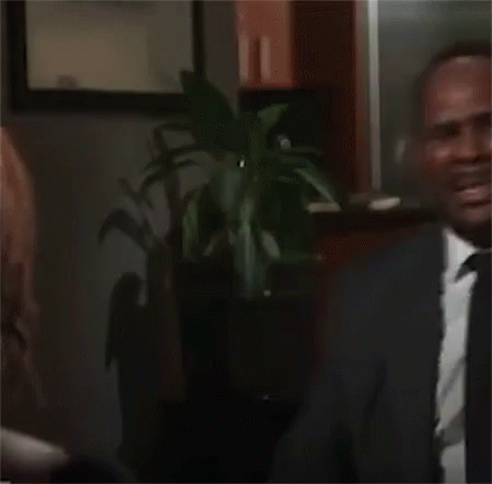 A Man In A Suit And Tie Is Dancing In Front Of A Man Sitting In A Chair . GIF