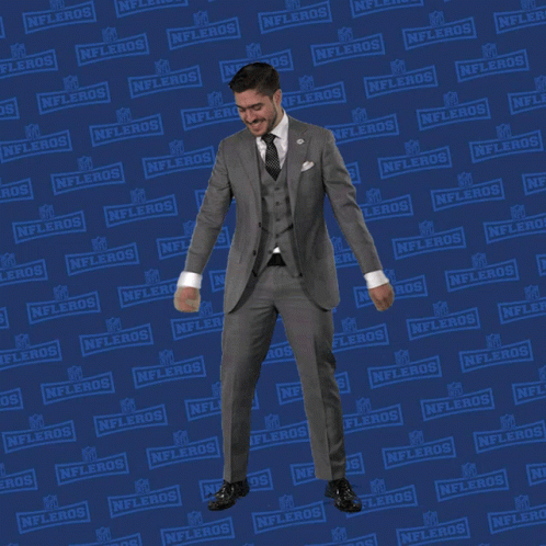 A Man In A Suit And Tie Is Dancing In Front Of A Nflers Sign GIF