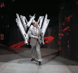 A Man In A Suit And Tie Is Dancing In Front Of A Wrestling Logo GIF