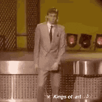 A Man In A Suit And Tie Is Dancing On A Stage In Front Of A Microphone . GIF