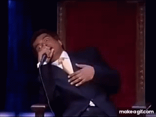A Man In A Suit And Tie Is Dancing On A Stage In Front Of A Microphone . GIF
