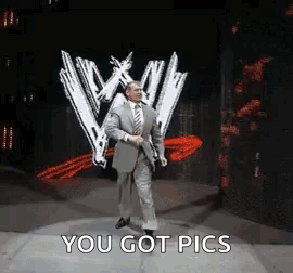 A Man In A Suit And Tie Is Dancing On A Stage In Front Of A Wwe Logo . GIF