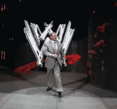 A Man In A Suit And Tie Is Dancing On A Stage In Front Of A Wwe Logo GIF