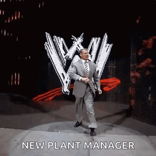 A Man In A Suit And Tie Is Dancing On A Stage With The Words `` New Plant Manager '' Written On It . GIF
