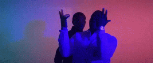 A Man In A Suit And Tie Is Dancing With His Arms In The Air In A Dark Room . GIF