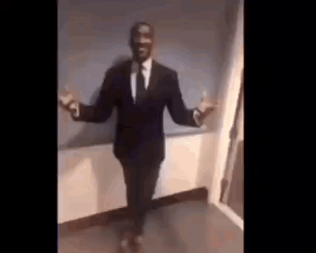 A Man In A Suit And Tie Is Dancing With His Arms Outstretched In A Room . GIF