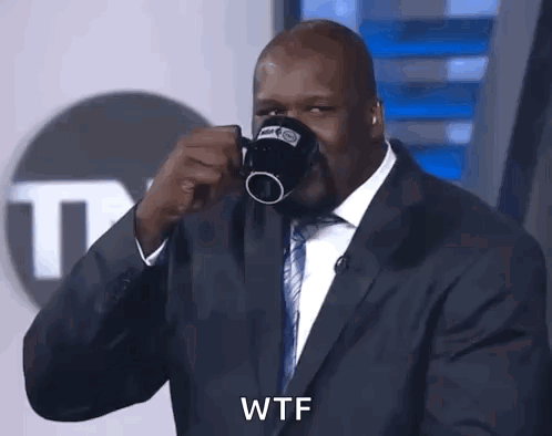 A Man In A Suit And Tie Is Drinking From A Coffee Mug And Says Wtf GIF