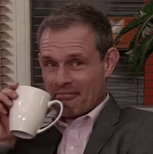 A Man In A Suit And Tie Is Drinking From A White Mug . GIF