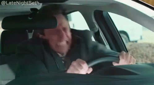 A Man In A Suit And Tie Is Driving A Car With A Caption That Says Latenightseth GIF
