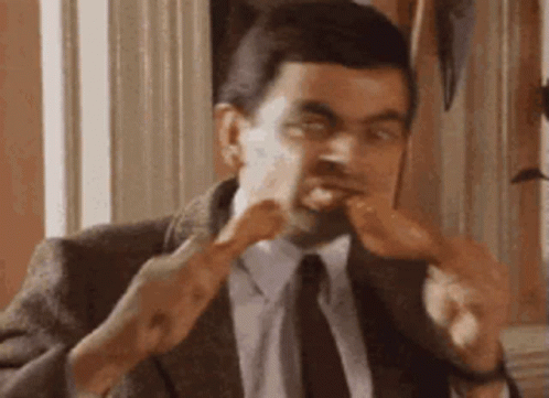 A Man In A Suit And Tie Is Eating A Chicken Wing . GIF