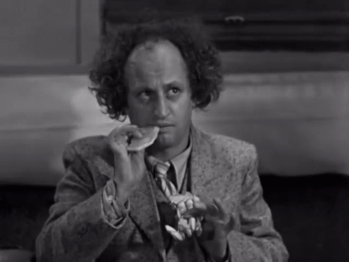 A Man In A Suit And Tie Is Eating A Piece Of Food GIF