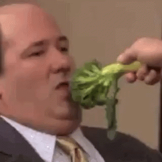 A Man In A Suit And Tie Is Eating Broccoli From A Person 'S Hand . GIF