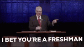 A Man In A Suit And Tie Is Giving A Speech In Front Of A Microphone And Pointing At The Audience . GIF