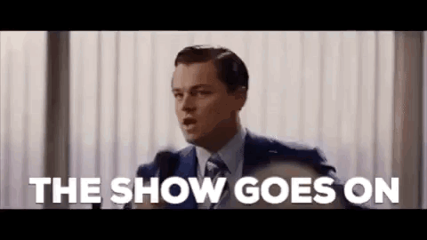 A Man In A Suit And Tie Is Giving A Speech In Front Of A Microphone And Saying The Show Goes On . GIF