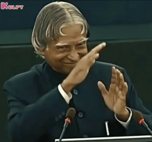 A Man In A Suit And Tie Is Giving A Speech In Front Of Microphones And Applauding . GIF