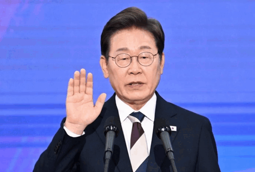 A Man In A Suit And Tie Is Giving A Speech In Front Of Two Microphones GIF