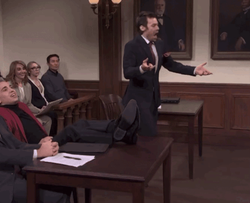 A Man In A Suit And Tie Is Giving A Speech To A Group Of People GIF
