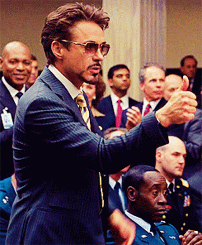 A Man In A Suit And Tie Is Giving A Thumbs Up In Front Of A Crowd GIF