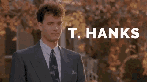A Man In A Suit And Tie Is Giving A Thumbs Up In Front Of A Sign That Says T. Hanks . GIF